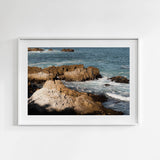 Framed wall art of rocky coastline with ocean waves on a white wall