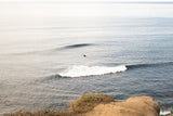 Lone surfer catching a wave in the ocean with cliffs in Sunset Cliffs, San Diego